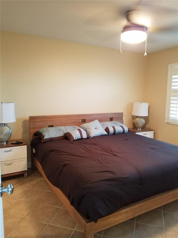 A bedroom features a wooden platform bed, two nightstands with lamps, and tile flooring — 1571 S ATLANTIC AVENUE UNIT 211, NEW SMYRNA BEACH, FL