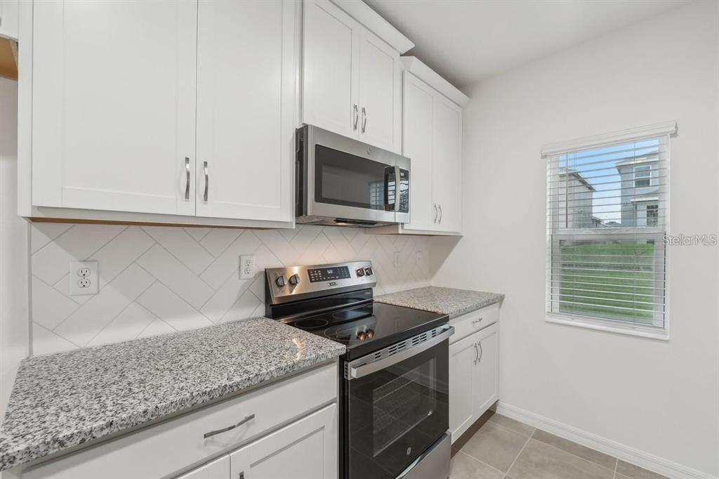 A kitchen features white cabinets, granite countertops, stainless steel appliances, and a herringbone tile backsplash — 434 NORTH BOULEVARD E, DAVENPORT, FL