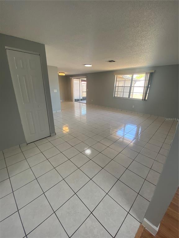 An open-concept living area features light-colored tile flooring, gray walls, and a sliding glass door — 12703 ALIDA PLACE, TAMPA, FL