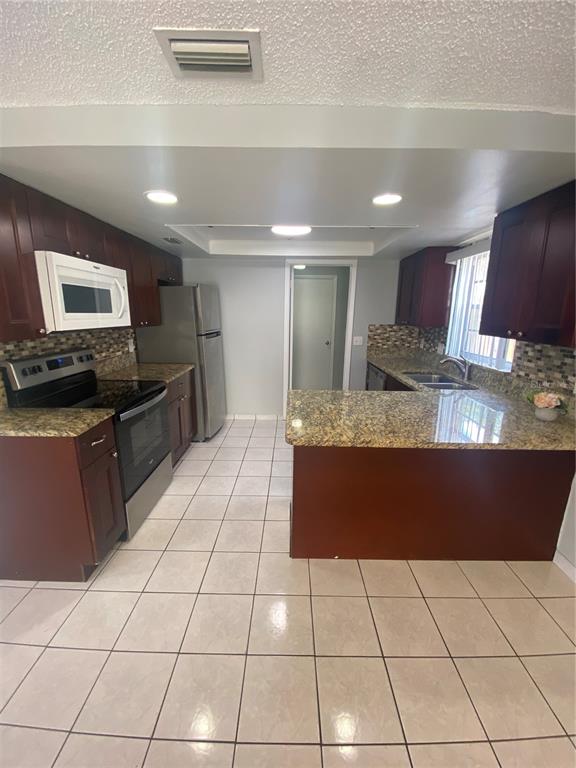 A kitchen features dark wood cabinets, granite countertops, stainless steel appliances, and light tile flooring — 12703 ALIDA PLACE, TAMPA, FL