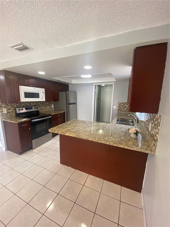 A kitchen with dark wood cabinets, granite countertops, stainless steel appliances, and tiled flooring — 12703 ALIDA PLACE, TAMPA, FL
