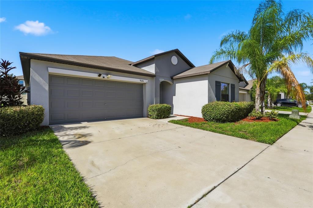 A single-story house with a gray garage, stucco exterior, and a palm tree in front — 9626 SAGE CREEK DRIVE, RUSKIN, FL