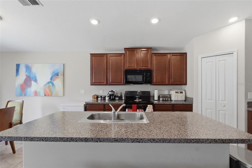 A kitchen features a granite-topped island with a sink, dark wood cabinets, and black appliances — 9626 SAGE CREEK DRIVE, RUSKIN, FL