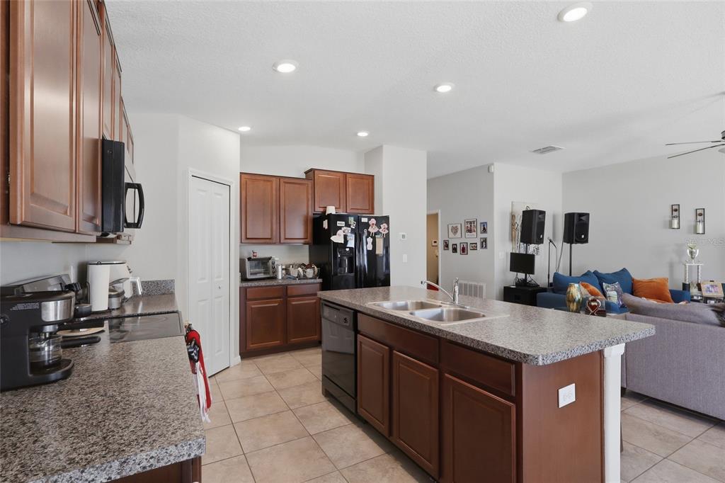 A kitchen with dark wood cabinets, granite countertops, and an island opens to a living area — 9626 SAGE CREEK DRIVE, RUSKIN, FL