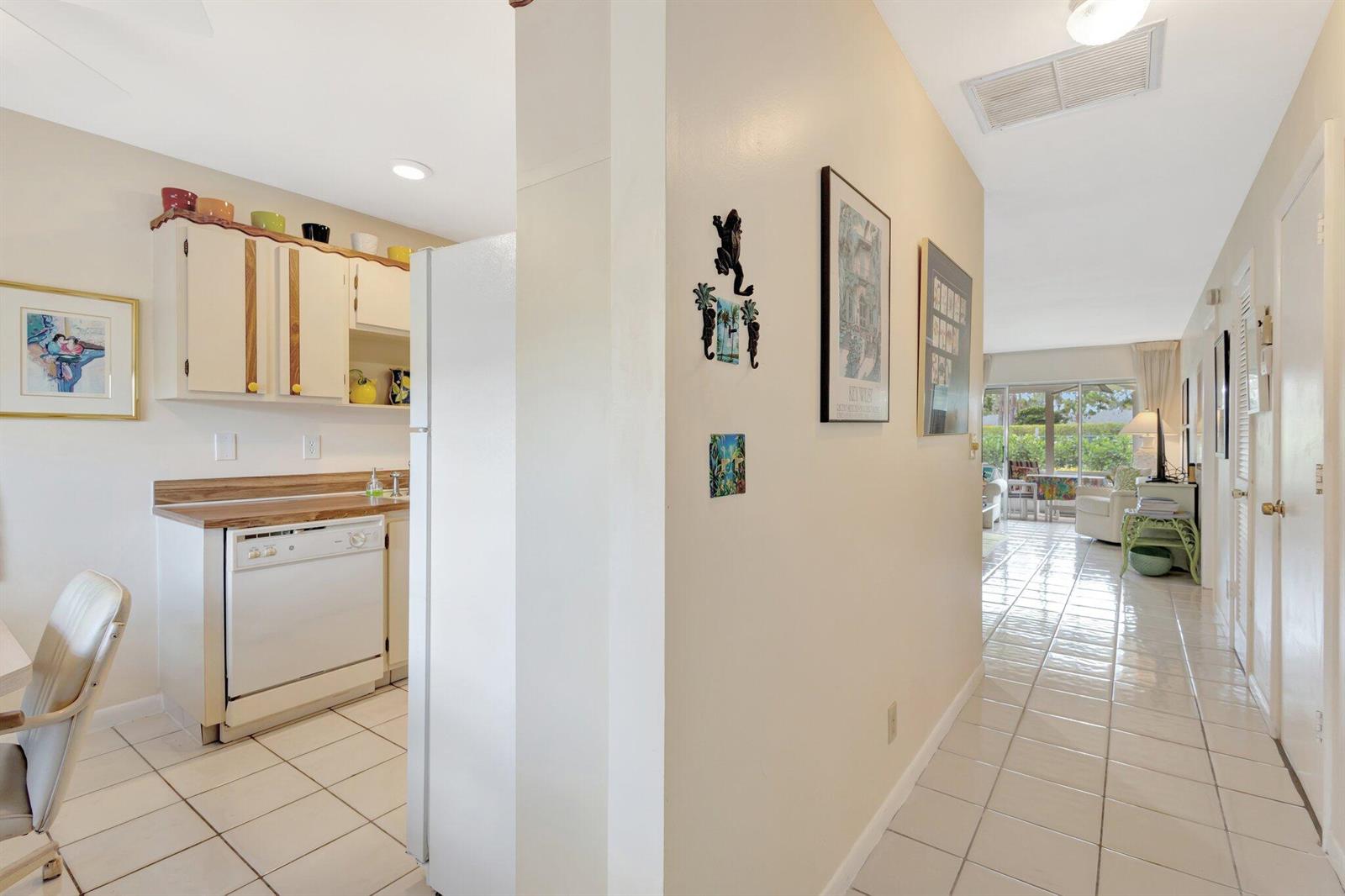 A kitchen with white cabinets and a dishwasher opens into a tiled hallway leading outside — 5200 Privet B Place # B, Delray Beach FL 33484, DELRAY BEACH, FL
