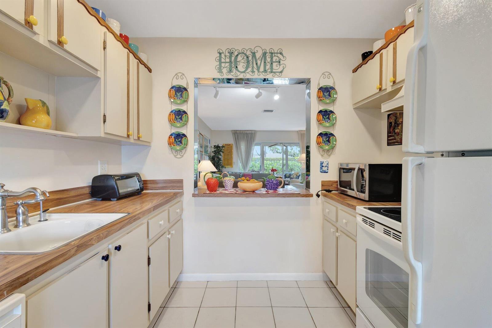 A galley kitchen features white cabinets, wood countertops, a pass-through window, and white tile flooring — 5200 Privet B Place # B, Delray Beach FL 33484, DELRAY BEACH, FL