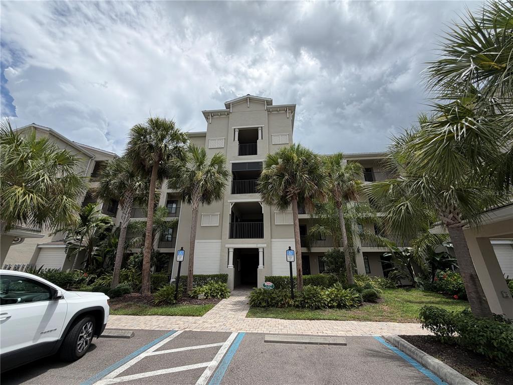 A multi-story apartment building exterior features a central entrance, balconies, and surrounding palm trees — 18008 GAWTHROP DRIVE UNIT 302, BRADENTON, FL
