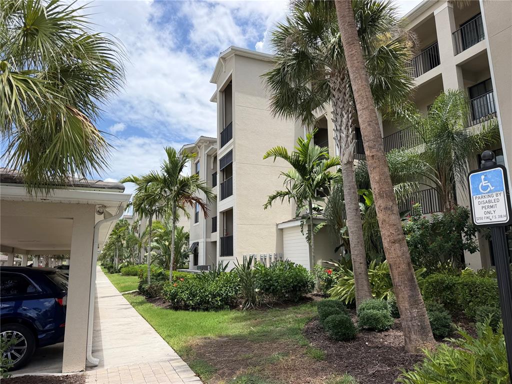 A view of a multi-story apartment building with palm trees and a handicap parking sign — 18008 GAWTHROP DRIVE UNIT 302, BRADENTON, FL