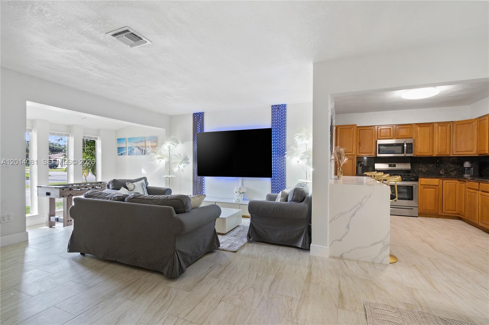 An open-concept living room with a large television and kitchen with wood cabinets — 2125 N 14th Ct, Hollywood FL 33020, HOLLYWOOD, FL