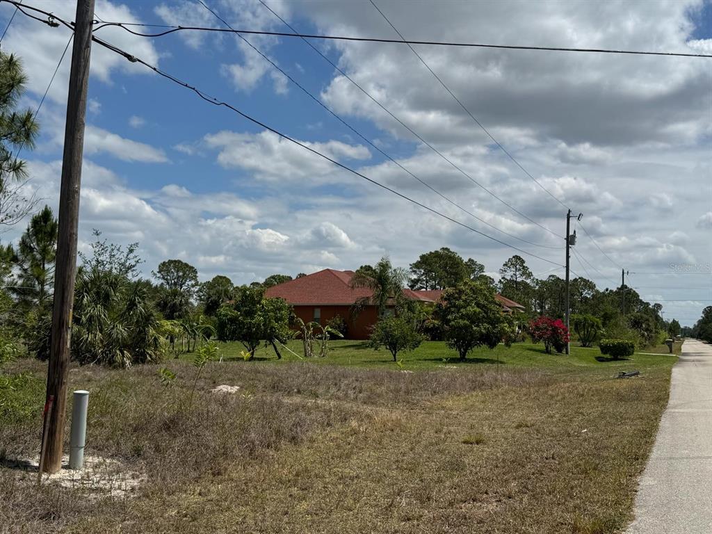 A red-roofed house sits on a grassy lot next to a paved road — 513 ADDISON STREET E, LEHIGH ACRES, FL