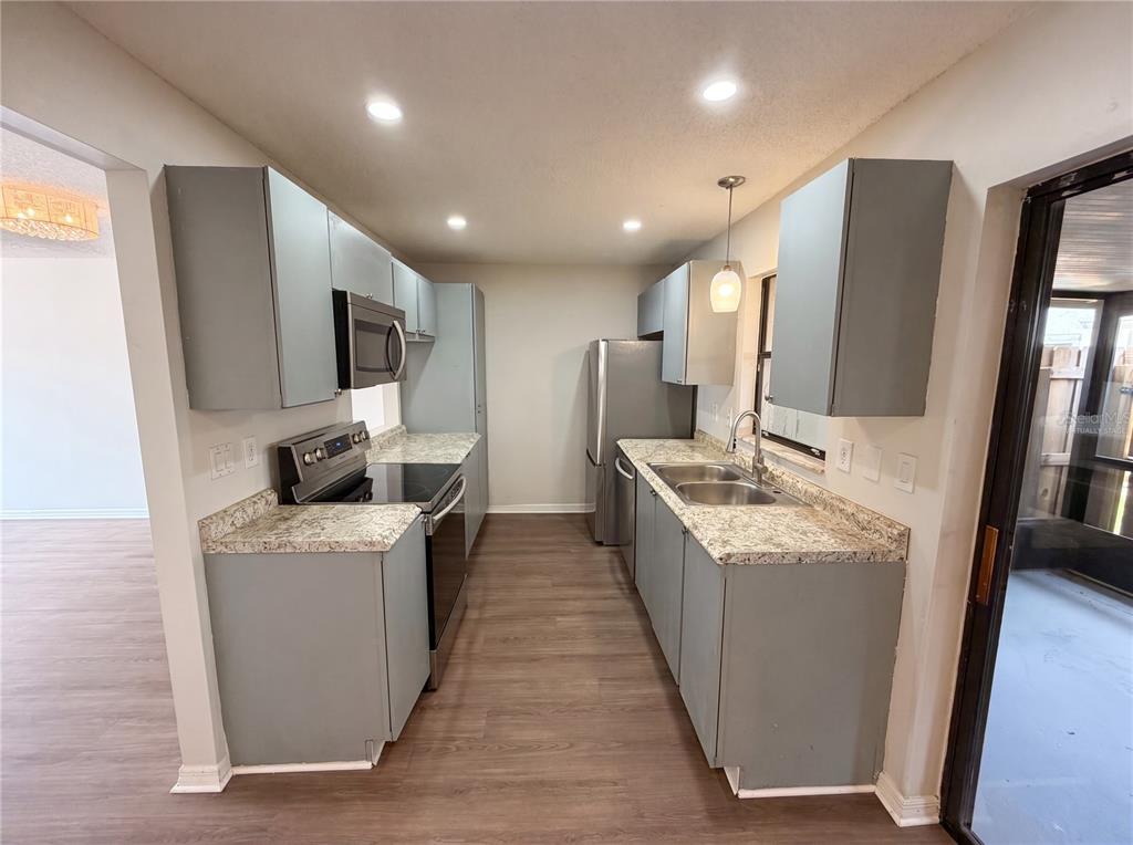 A galley kitchen features gray cabinets, granite countertops, stainless steel appliances, and wood-look flooring — 1602 LITTLE FALLS CIRCLE UNIT 75, ORLANDO, FL