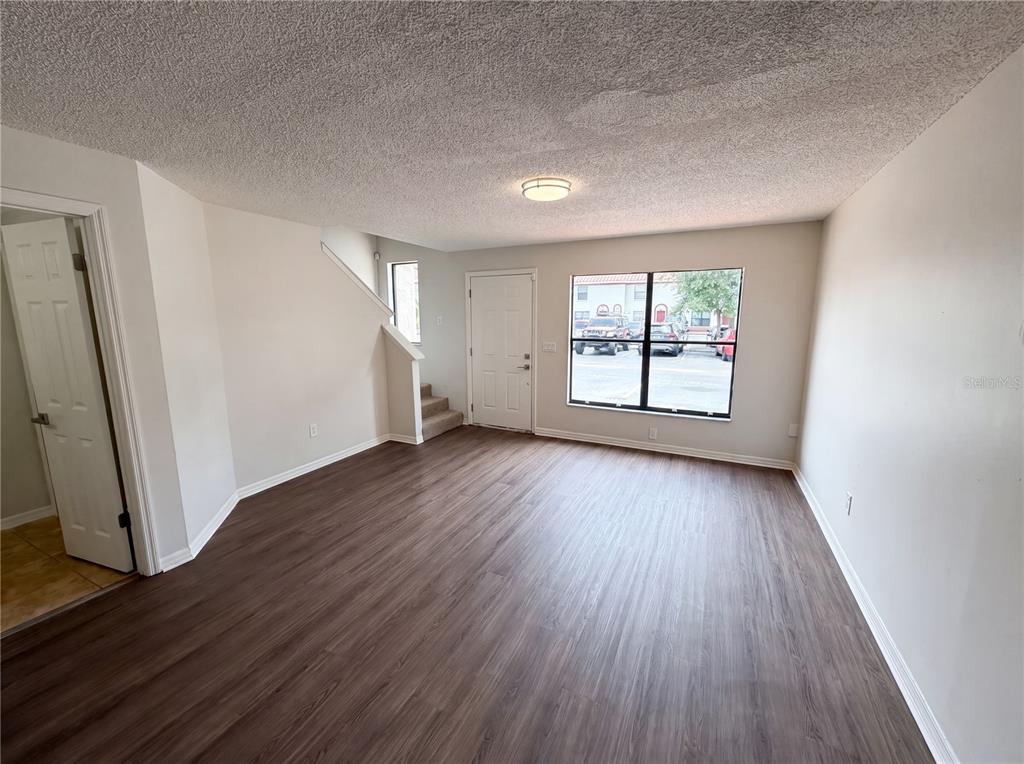 An empty living room features wood-look flooring, white walls, a staircase, and a large window — 1602 LITTLE FALLS CIRCLE UNIT 75, ORLANDO, FL