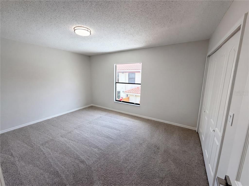An empty bedroom features light gray walls, beige carpeting, a ceiling light, and a closet — 1602 LITTLE FALLS CIRCLE UNIT 75, ORLANDO, FL