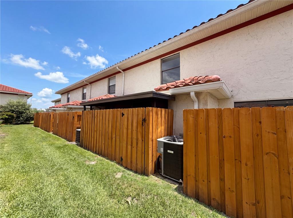 A wooden fence encloses the back patio and air conditioning unit of a stucco townhouse — 1602 LITTLE FALLS CIRCLE UNIT 75, ORLANDO, FL