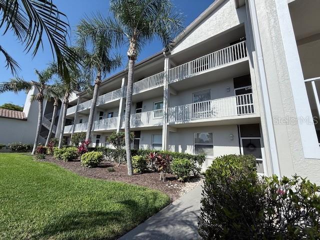 A three-story apartment building features white stucco walls, balconies, and palm trees on a lawn — 8755 OLDE HICKORY AVENUE UNIT 7109, SARASOTA, FL