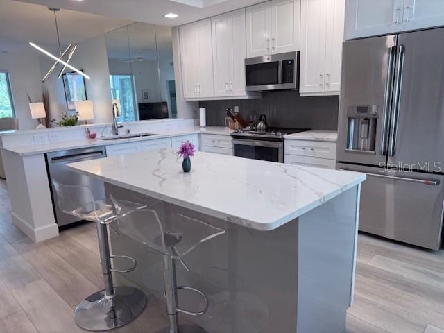 A modern kitchen features white cabinets, a marble-topped island with stools, and stainless steel appliances — 8755 OLDE HICKORY AVENUE UNIT 7109, SARASOTA, FL