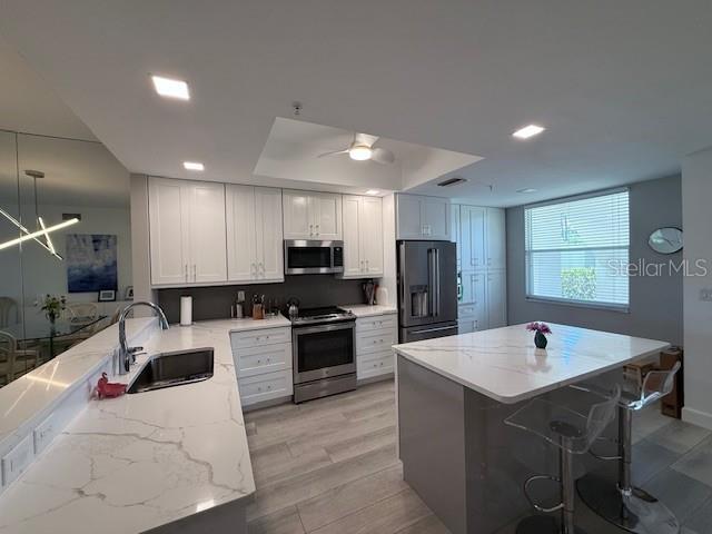 A modern kitchen features white cabinetry, stainless steel appliances, and a large marble-topped island — 8755 OLDE HICKORY AVENUE UNIT 7109, SARASOTA, FL