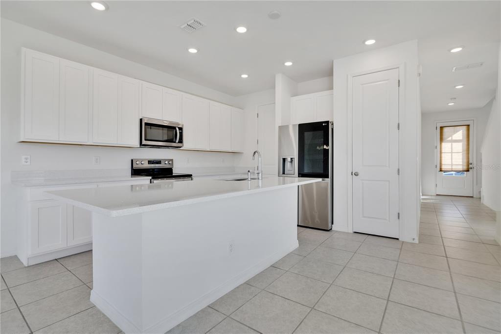 A modern kitchen features white cabinetry, a large island, stainless steel appliances, and tile flooring — 1484 DISCOVERY STREET, DAVENPORT, FL