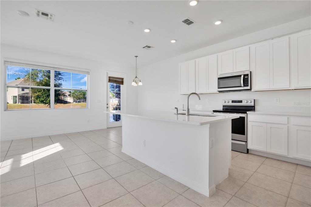 A bright kitchen features white cabinets, a central island, stainless steel appliances, and tile flooring — 1484 DISCOVERY STREET, DAVENPORT, FL