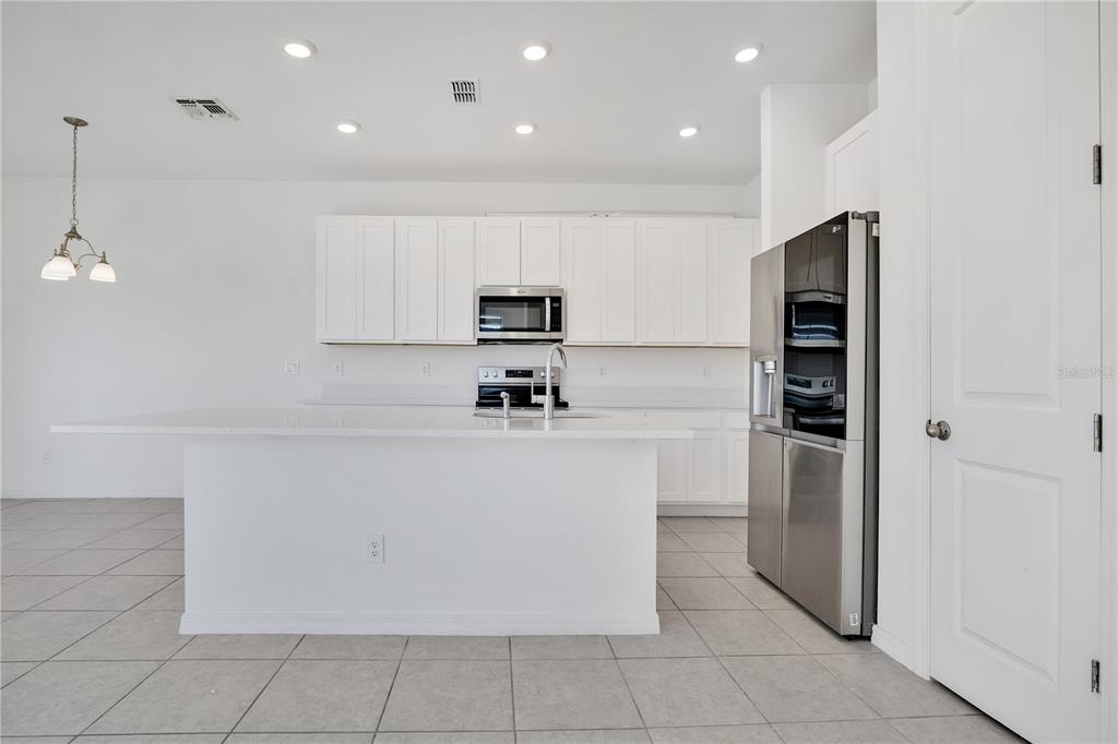 A modern kitchen features white cabinetry, a large island, stainless steel appliances, and tile flooring — 1484 DISCOVERY STREET, DAVENPORT, FL
