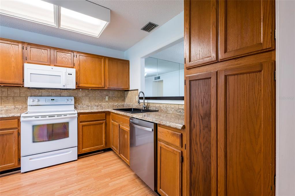 A kitchen features wood cabinets, granite countertops, a white stove, and a stainless steel dishwasher — 3164 VALLEY OAKS DRIVE UNIT 3164, TAMPA, FL