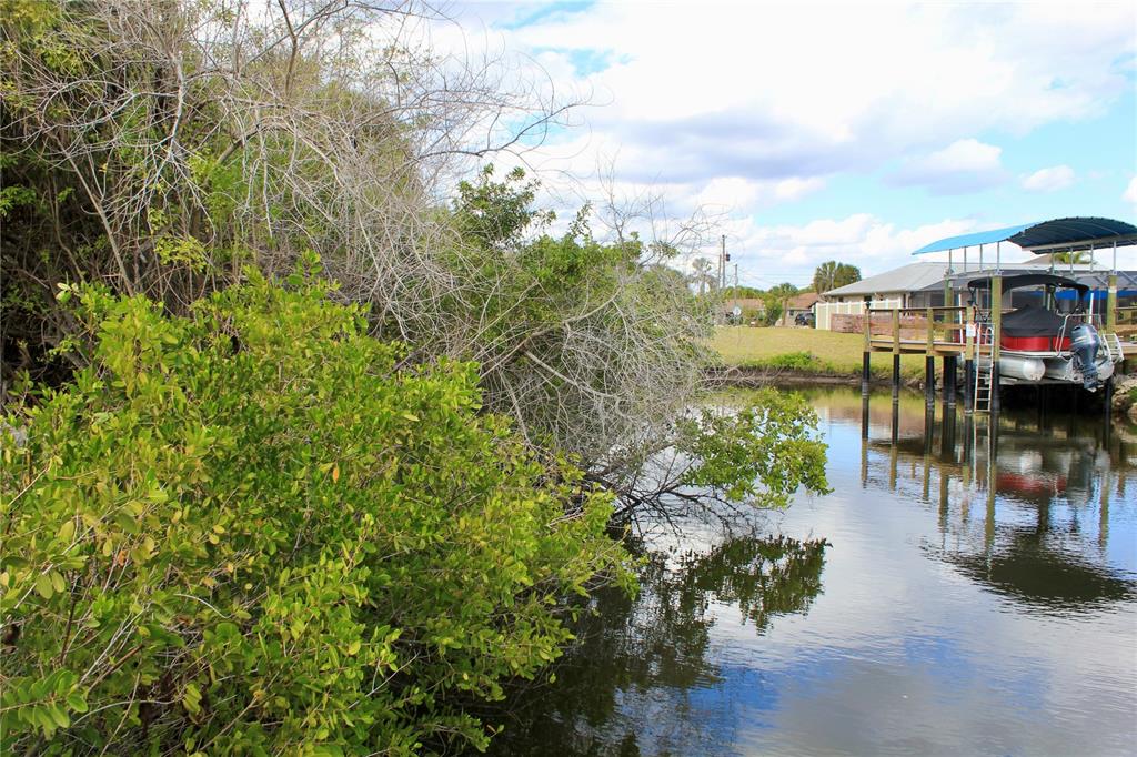 A canal view showing a boat lift with a pontoon boat and dense shoreline vegetation — 4402,4410 BAYVIEW STREET, PORT CHARLOTTE, FL