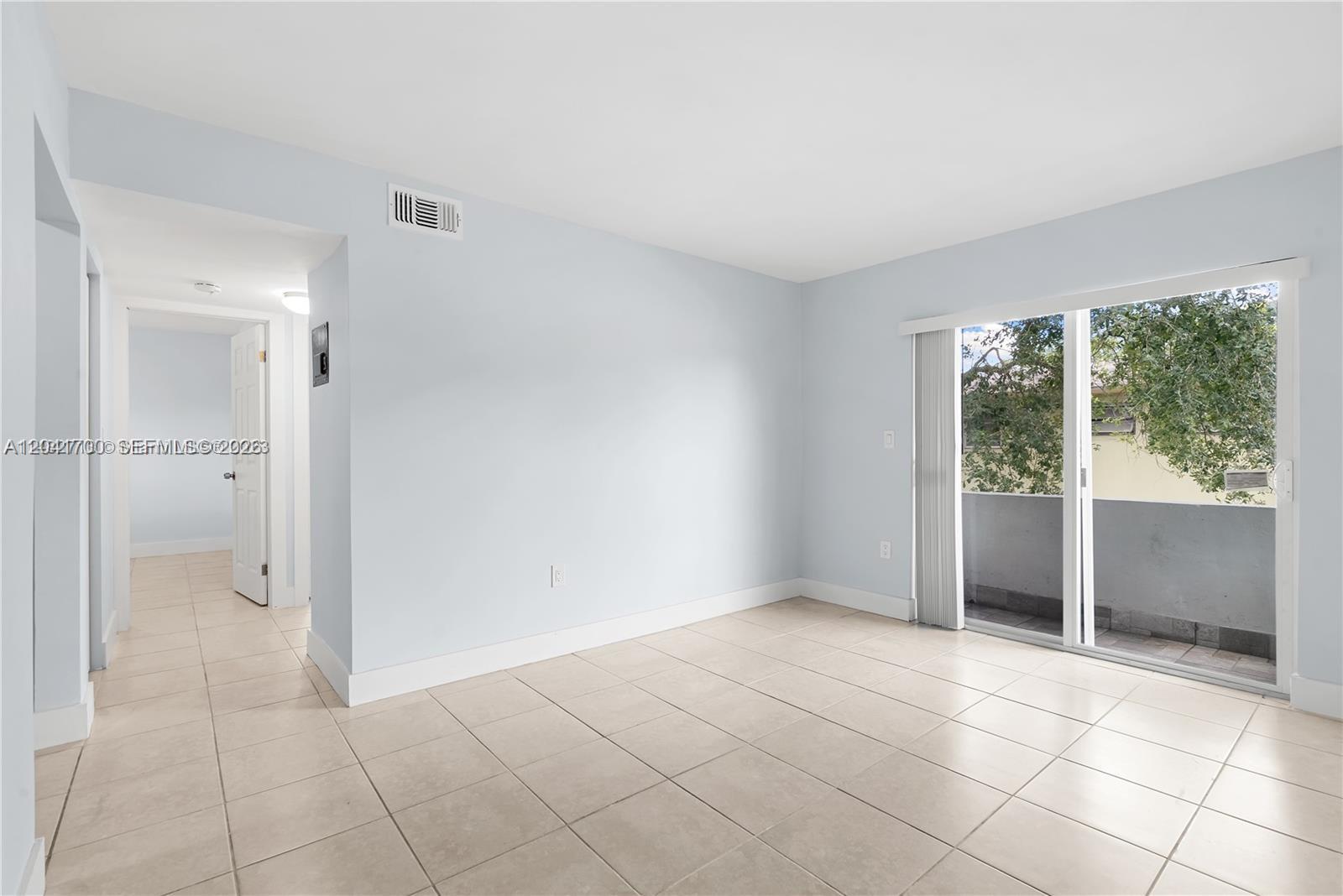 An empty room features light-colored tile flooring, pale blue walls, and a sliding glass door — 7722 NE 3rd Ct # 2, Miami FL 33138, MIAMI, FL