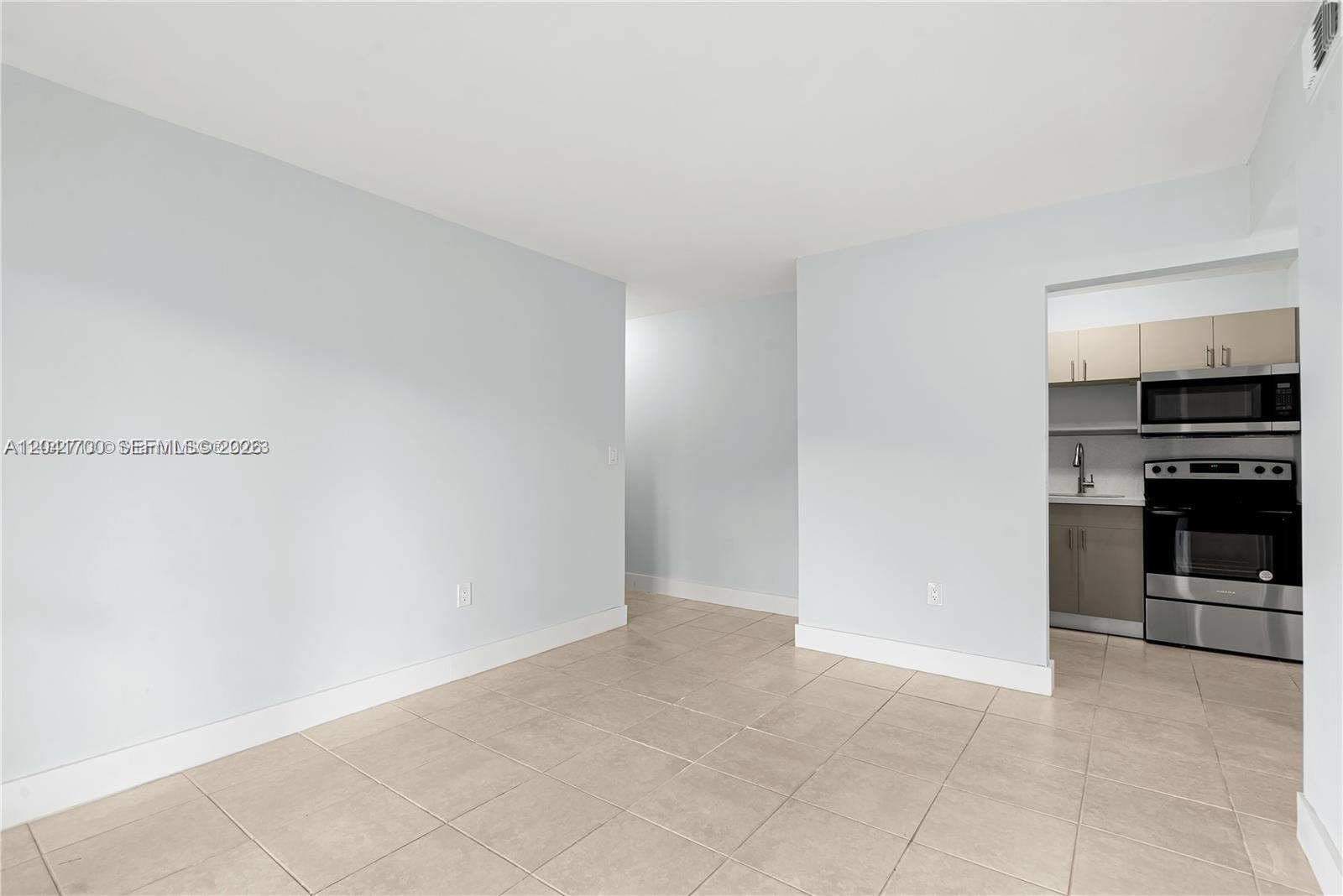 An empty room with light-colored tile flooring leads to a small kitchen with stainless appliances — 7722 NE 3rd Ct # 2, Miami FL 33138, MIAMI, FL