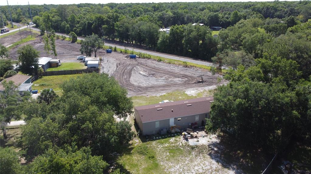 An aerial view shows a house with a brown roof next to a cleared dirt lot — 6590 OSCEOLA POLK LINE ROAD, DAVENPORT, FL