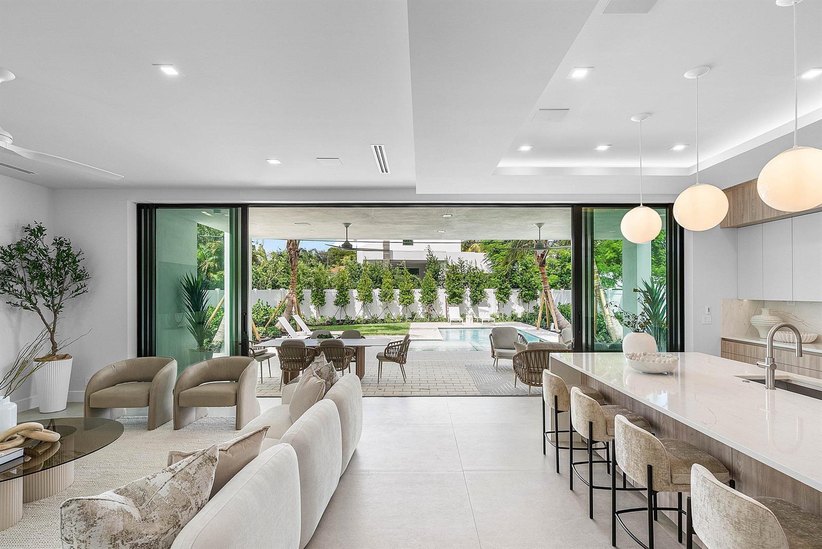 A modern open-concept living area features a kitchen island, lounge seating, and large sliding doors — 721 Lake Avenue N, Delray Beach FL 33483, DELRAY BEACH, FL