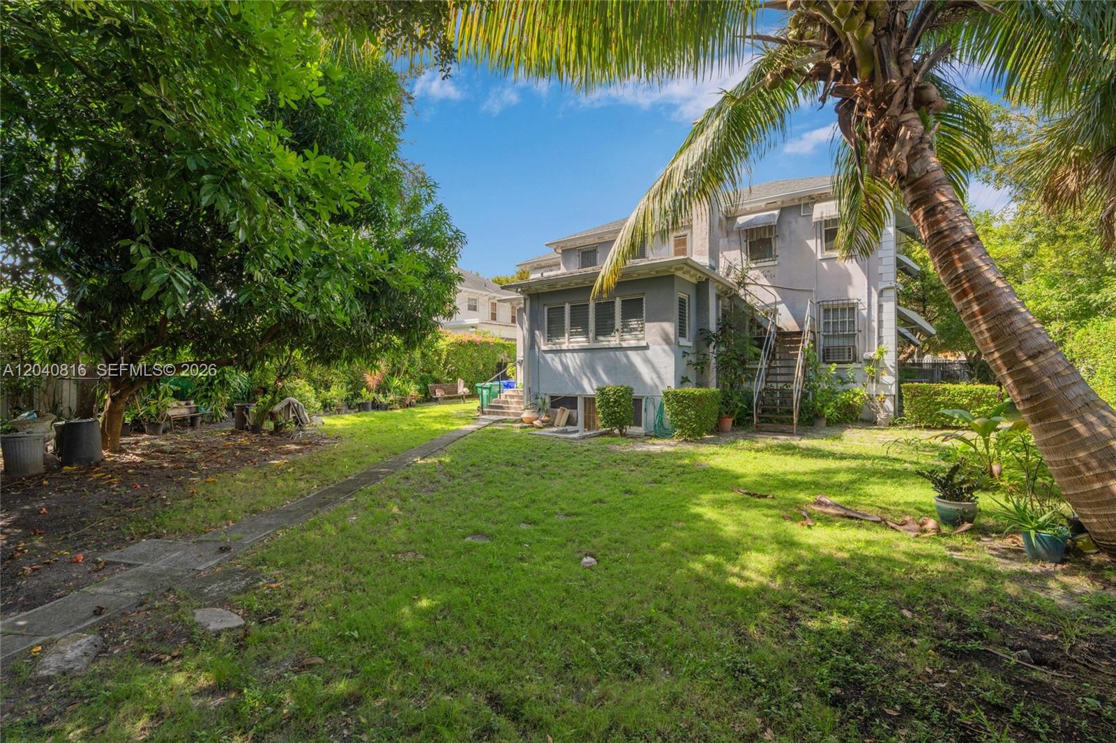 A backyard features a grassy lawn, a palm tree, and a multi-story gray house — 405 SW 11th Ave, Miami FL 33130, MIAMI, FL