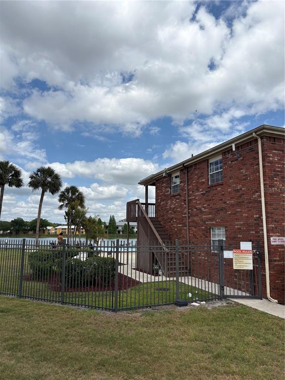 A brick apartment building exterior features an outdoor staircase leading to a fenced pool area — 1920 E EDGEWOOD DRIVE UNIT I 10, LAKELAND, FL