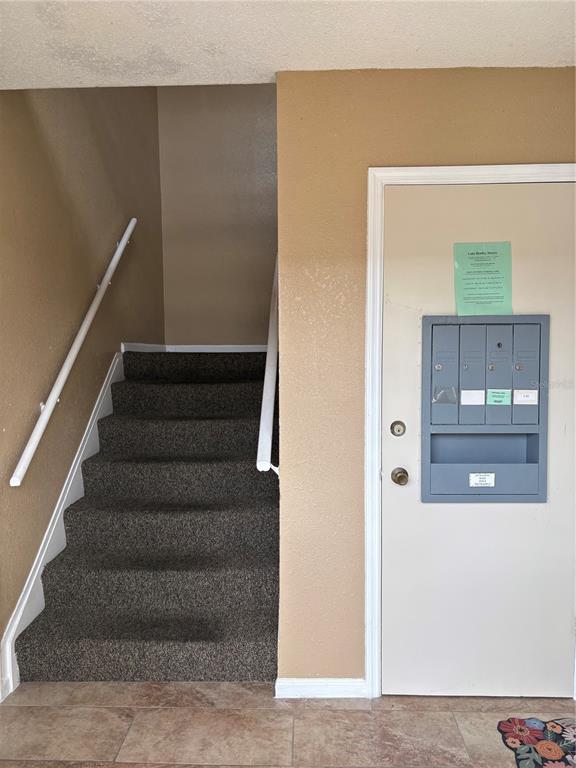 A carpeted staircase sits beside a door featuring a wall-mounted mail collection unit — 1920 E EDGEWOOD DRIVE UNIT I 10, LAKELAND, FL