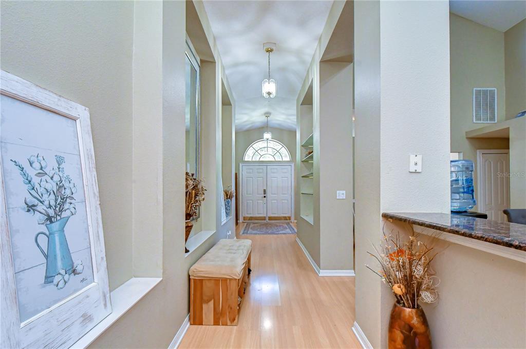 A bright entryway features light wood flooring, a bench, and a view of the front door — 9244 BRINDLEWOOD DRIVE, ODESSA, FL
