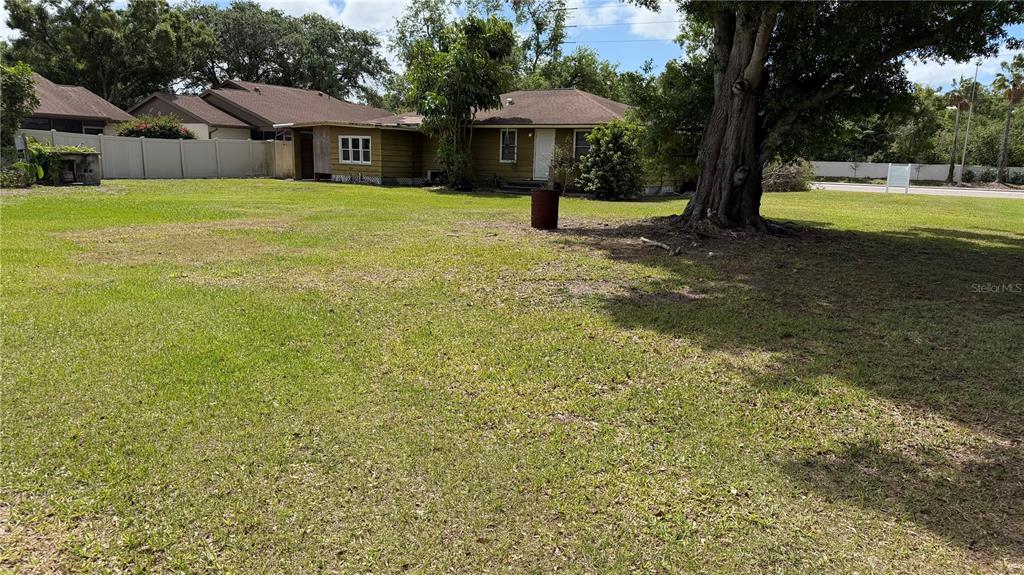 A large grassy yard leads to the back of a single-story house with brown siding — 4611 FRUITVILLE ROAD, SARASOTA, FL