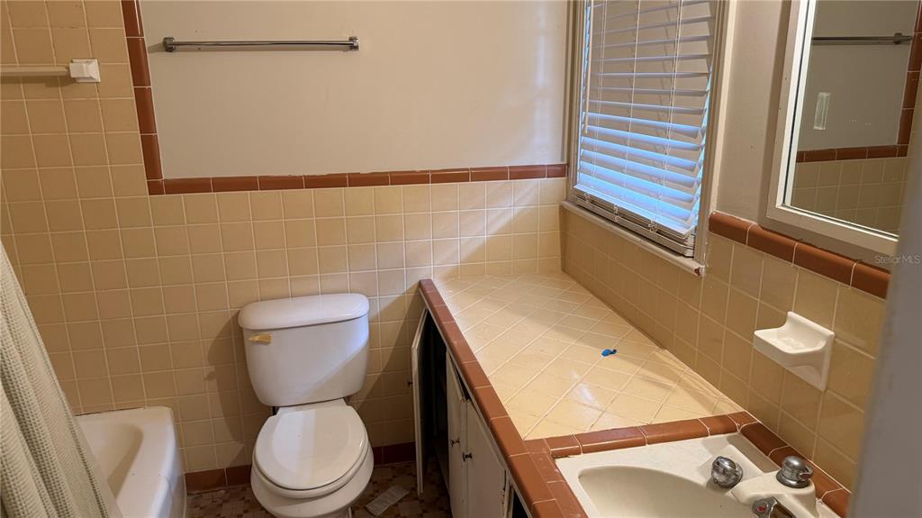 A bathroom features tan tiled walls, a white toilet, and a tiled vanity countertop — 4611 FRUITVILLE ROAD, SARASOTA, FL
