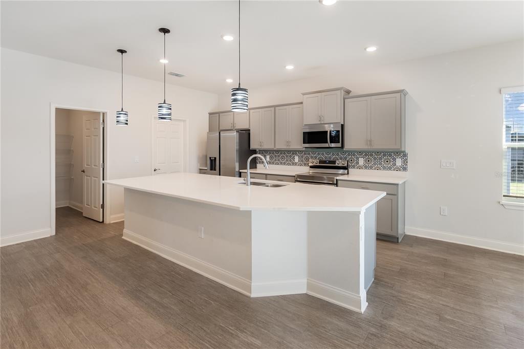 A modern kitchen features a large white island, grey cabinetry, and patterned tile backsplash — 1348 MELROSE STREET, LAKE ALFRED, FL