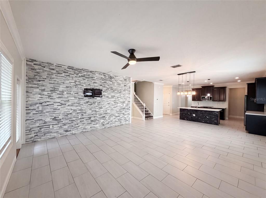 An open-concept living area features a stone accent wall, tile flooring, and a modern kitchen — 1423 PRO SHOP COURT, DAVENPORT, FL