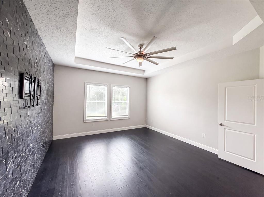 A bedroom features dark wood flooring, a textured accent wall, and a tray ceiling — 1423 PRO SHOP COURT, DAVENPORT, FL