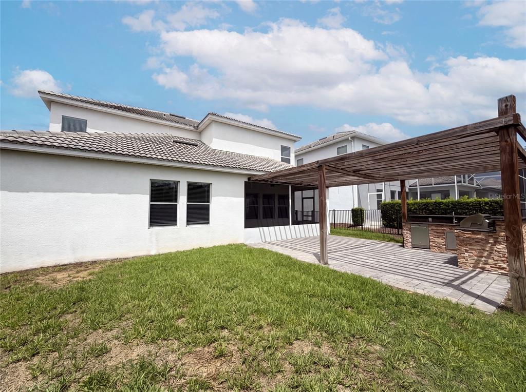 A backyard features a paved patio, a wooden pergola, and an outdoor kitchen area — 1423 PRO SHOP COURT, DAVENPORT, FL