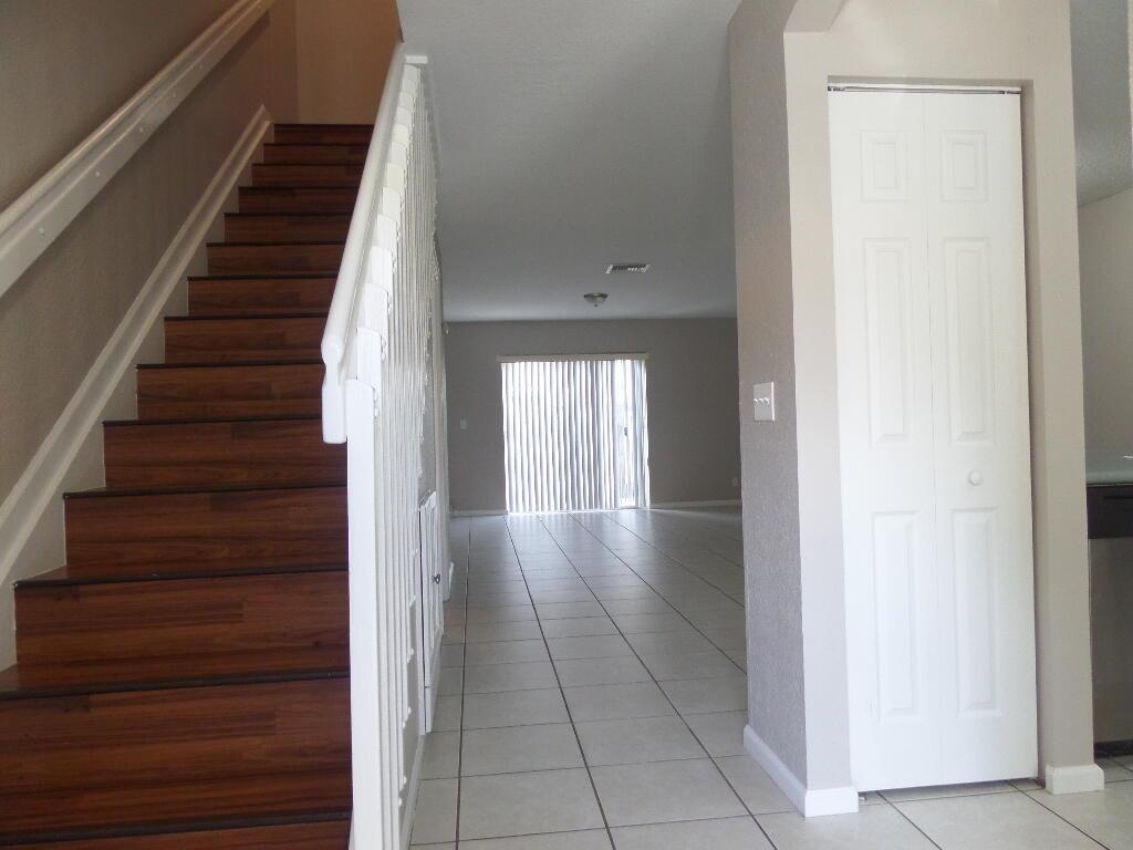 A view of an entryway with wood-tread stairs, white railings, and tile flooring leading to a patio door — 862 Summit Lake Drive, West Palm Beach FL 33406, WEST PALM BEACH, FL