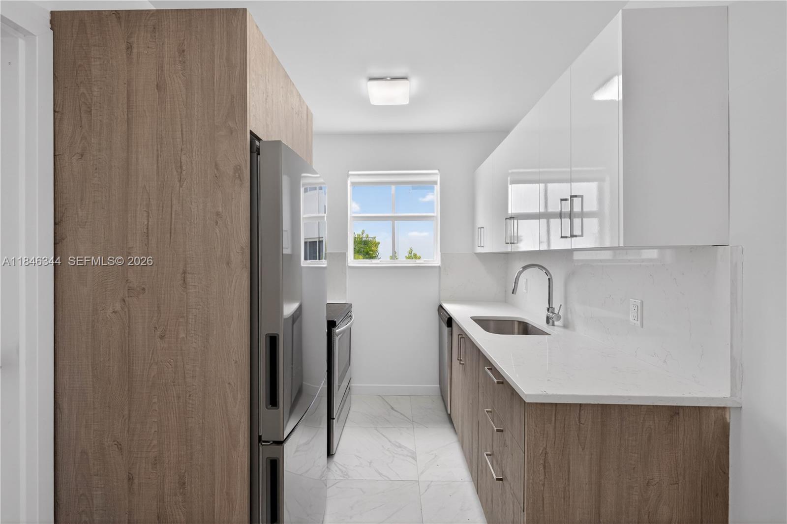 A galley kitchen features wood-grain lower cabinets, white upper cabinets, and white marble-look countertops — 1552 Euclid Ave # 4, Miami Beach FL 33139, MIAMI BEACH, FL