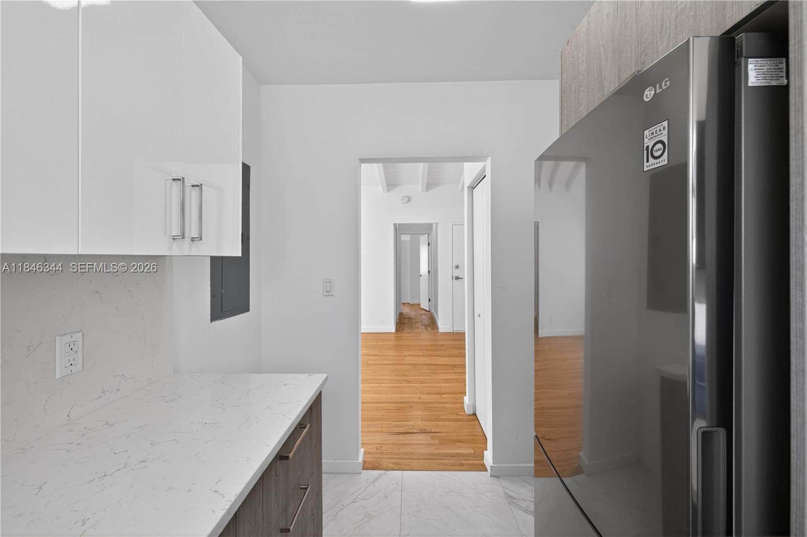 A kitchen features white upper cabinets, wood-tone lower cabinets, marble-look countertops, and a stainless steel refrigerator — 1552 Euclid Ave # 4, Miami Beach FL 33139, MIAMI BEACH, FL