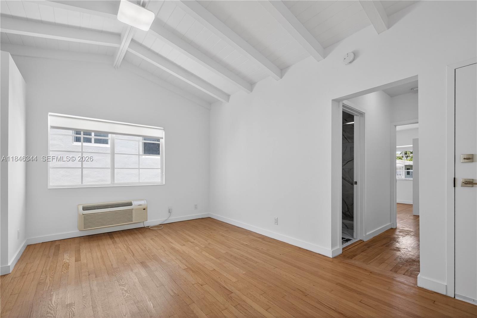 An empty room features white walls, a vaulted ceiling with exposed beams, and hardwood floors — 1552 Euclid Ave # 4, Miami Beach FL 33139, MIAMI BEACH, FL