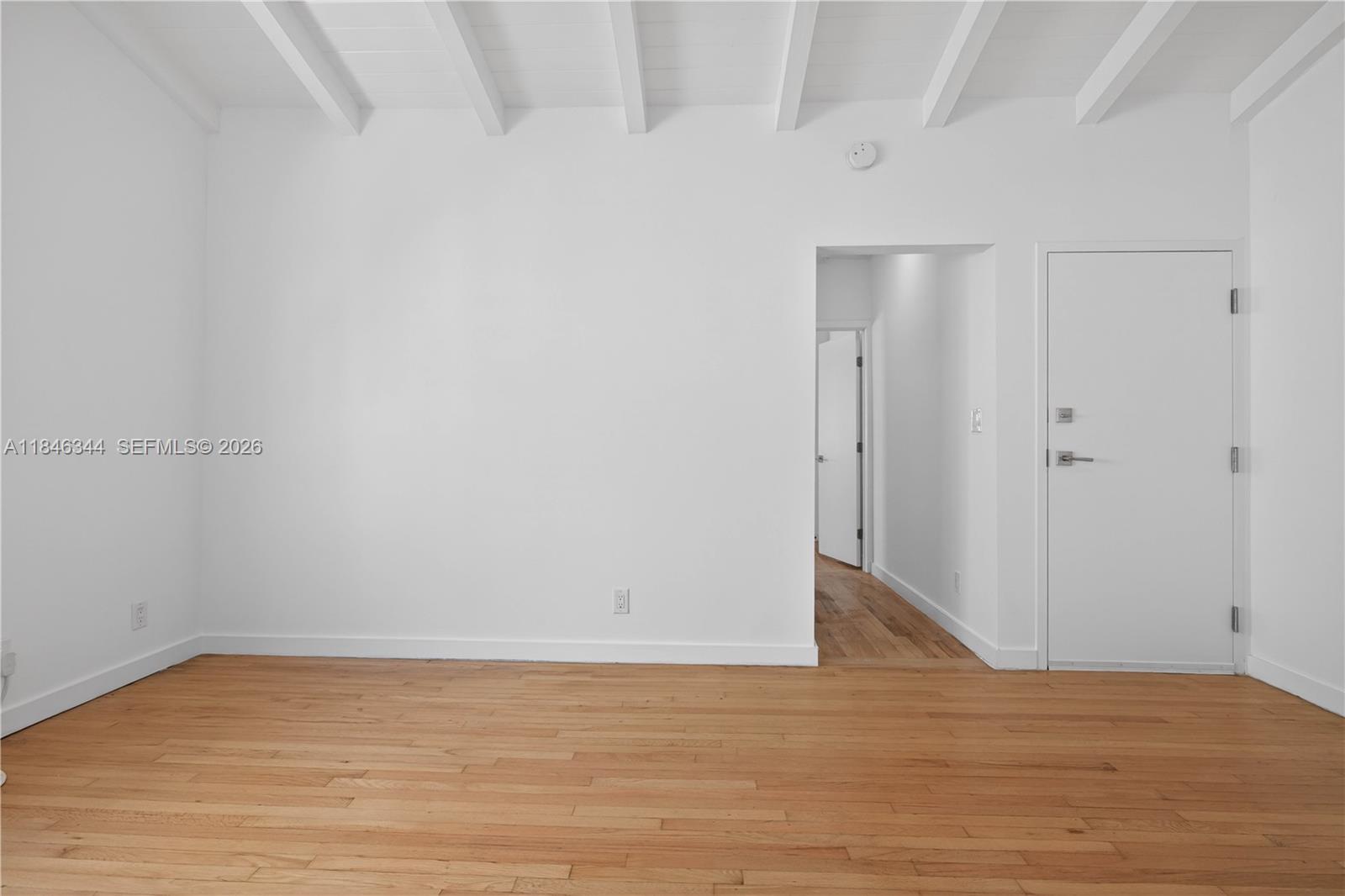 An empty room features white walls, a vaulted ceiling with beams, and hardwood flooring — 1552 Euclid Ave # 4, Miami Beach FL 33139, MIAMI BEACH, FL