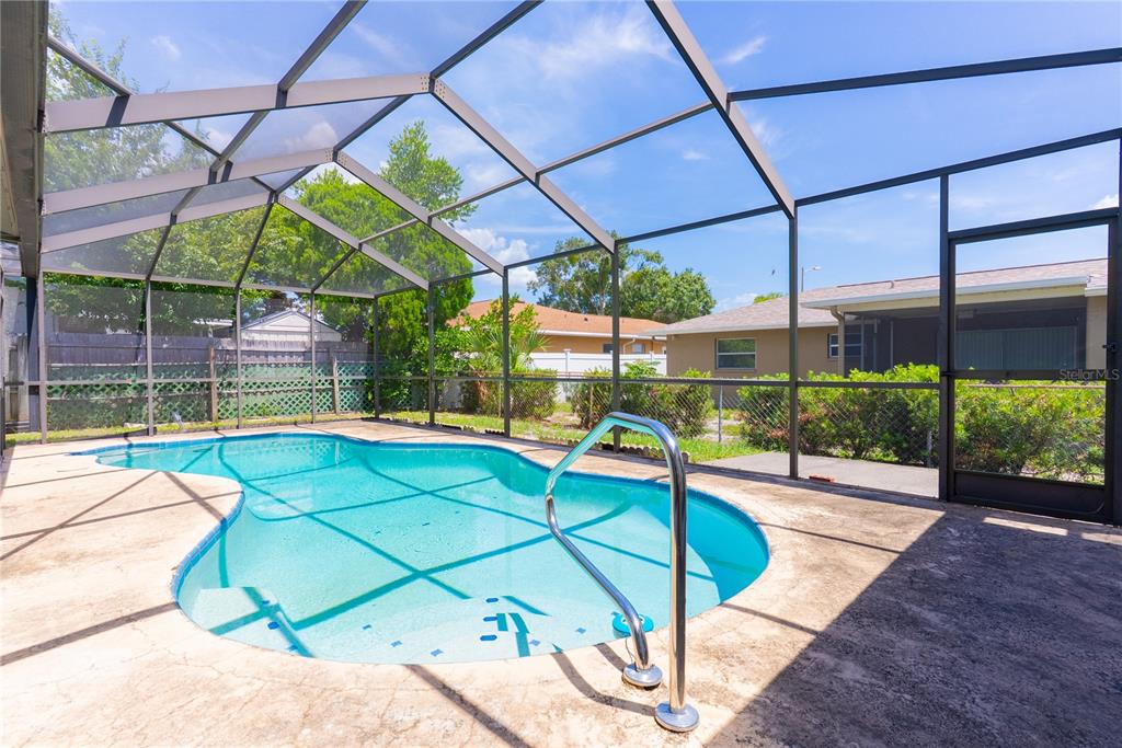 A screened-in backyard swimming pool with a concrete deck and metal handrail — 8234 WINTHROP DRIVE, PORT RICHEY, FL
