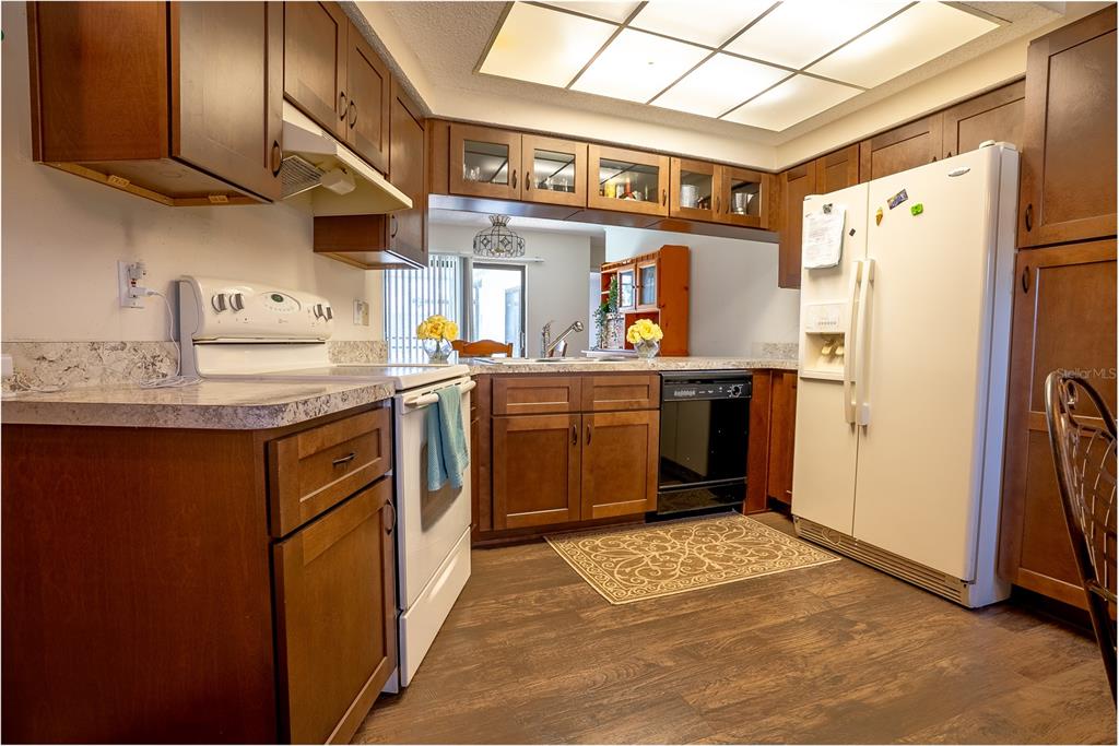 A kitchen features wood cabinets, white appliances, a patterned rug, and a drop ceiling light — 8234 WINTHROP DRIVE, PORT RICHEY, FL