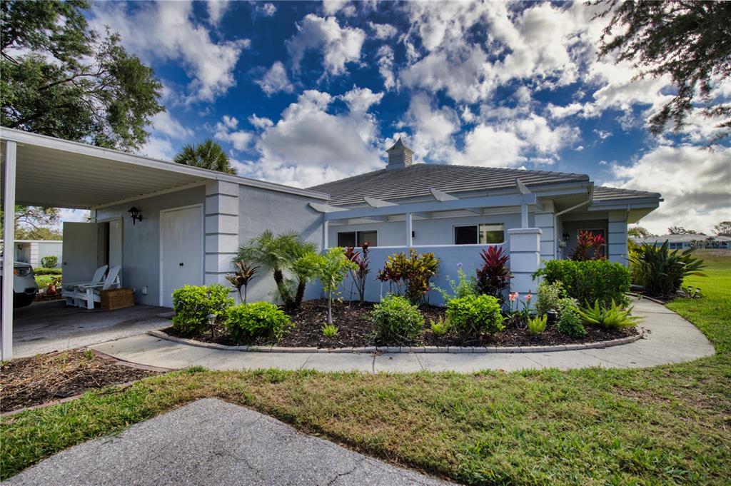 Exterior view of a single-story house with a carport, landscaping, and a tiled roof — 208 CERROMAR WAY S UNIT 26, VENICE, FL