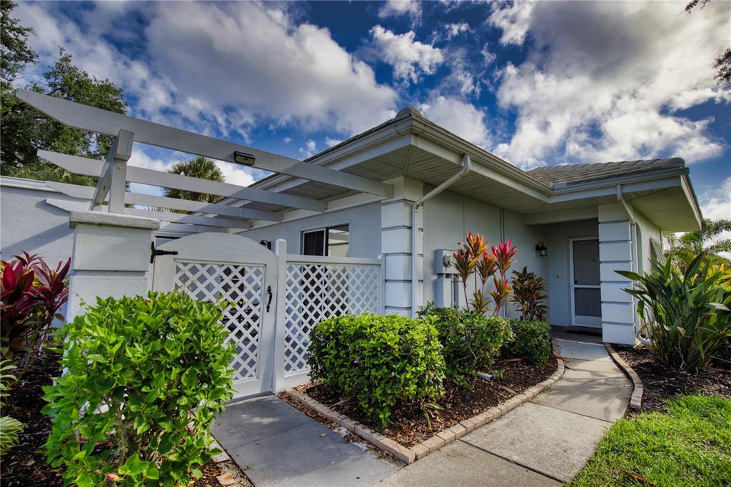 The exterior of a light-colored house features a white lattice gate and a pergola — 208 CERROMAR WAY S UNIT 26, VENICE, FL