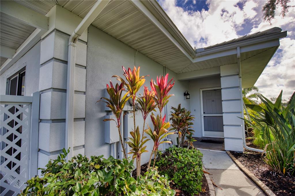 A concrete walkway leads to the front entrance of a house with tropical landscaping — 208 CERROMAR WAY S UNIT 26, VENICE, FL